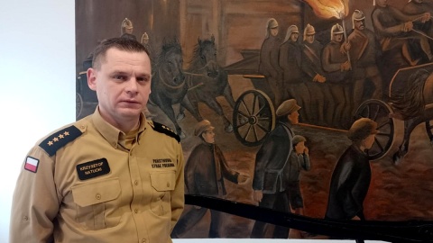 Komendant Jednostki Ratowniczo Gaśniczej w Brodnicy, st. kpt. mgr Krzysztof Natucki przy obrazie Edmunda Czerwińskiego. Fot. Michał Zaręba/PR PiK