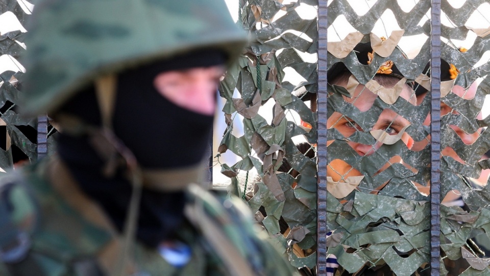Uzbrojony mężczyzna (najprawdopodobniej rosyjski żołnierz) przed bramą ukraińskiej jednostki w Sewastopolu. Fot. PAP/EPA.