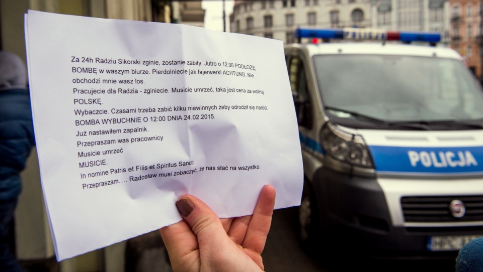 Policyjne samochody przed biurem w Bydgoszczy, na pierwszym planie kartka z pogróżkami. Fot. PAP/Tytus Żmijewski