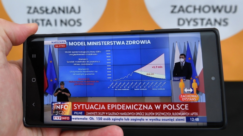 Transmisja konferencji prasowej z udziałem dyrektora Narodowego Instytutu Zdrowia Publicznego – Państwowego Zakładu Higieny Grzegorza Juszczyka (na ekranie telefonu) z KPRM w Warszawie. Fot. PAP/Radek Pietruszka