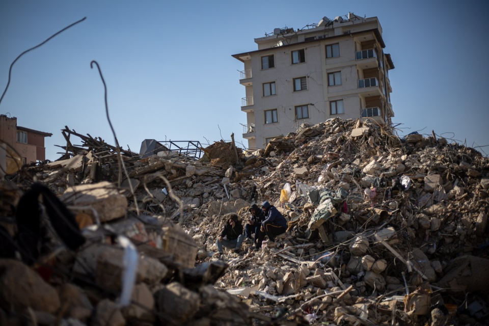 Ludzie siedzący na gruzach zawalonego budynku w Hatay w Turcji, 14 lutego 2023 roku/fot. Martin Divisek, PAP/EPa