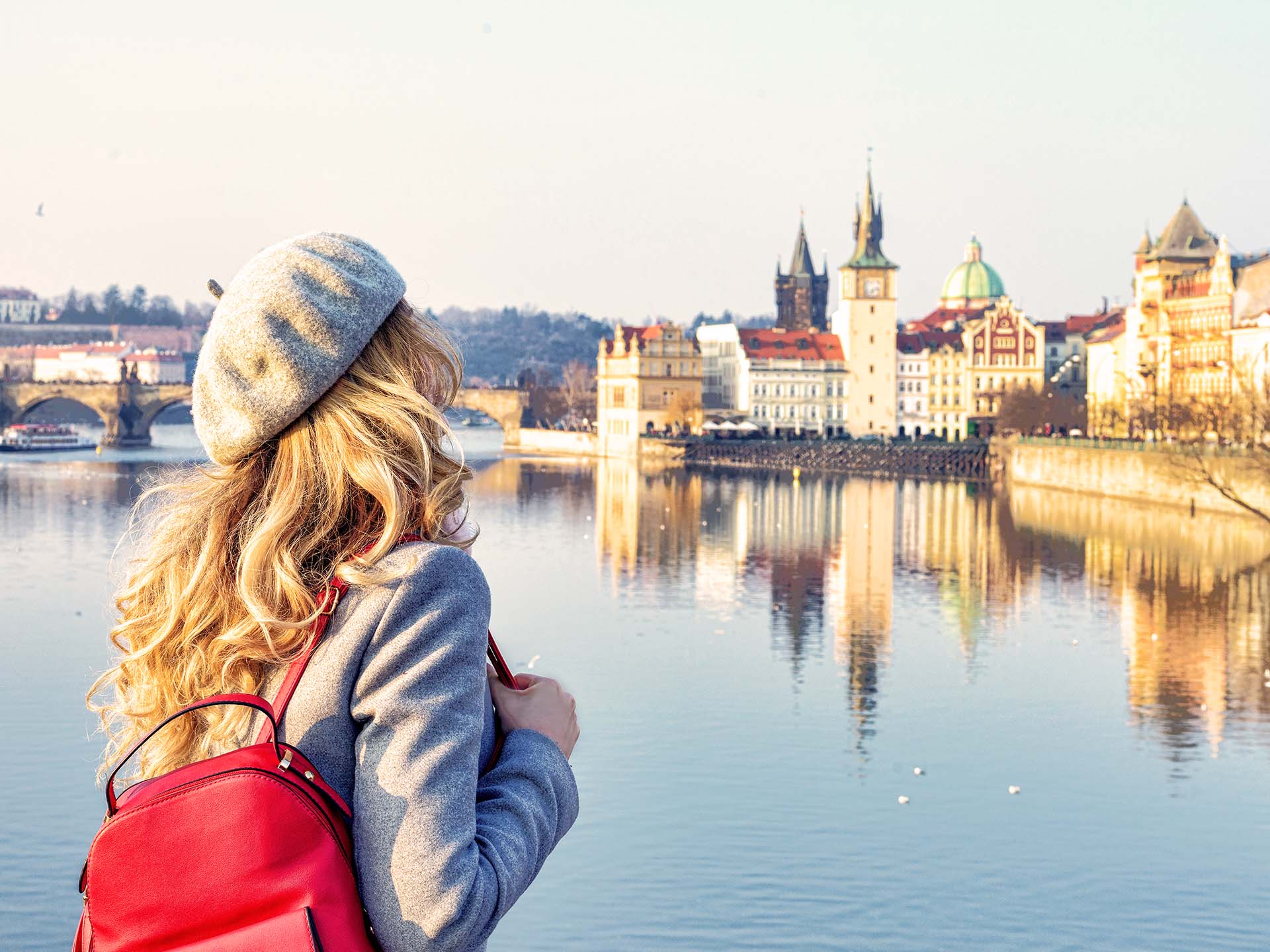 Kobieta z czerwonym plecakiem patrząca na panoramę Pragi nad Wełtawą.
